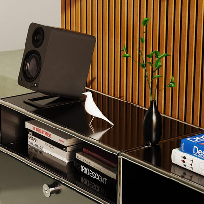 Matte black powered speaker tilted on shelf, showing woofer and tweeter