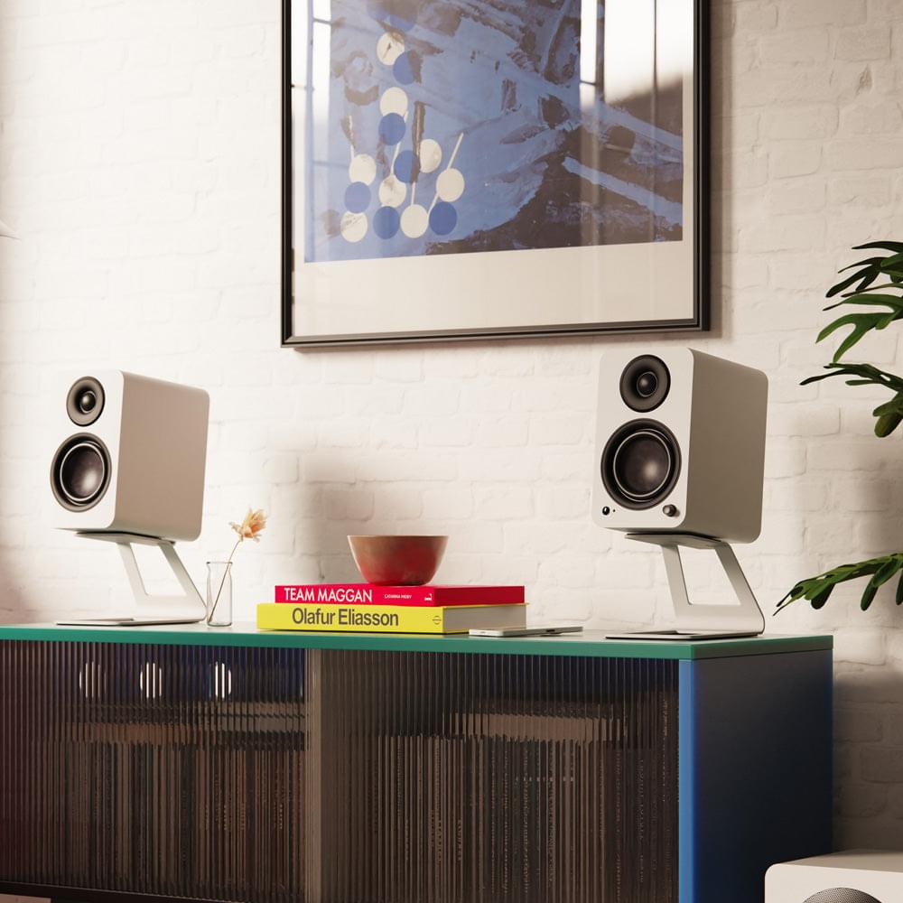 Pair of matte white powered bookshelf speakers on a shelf, angled front with black drivers.