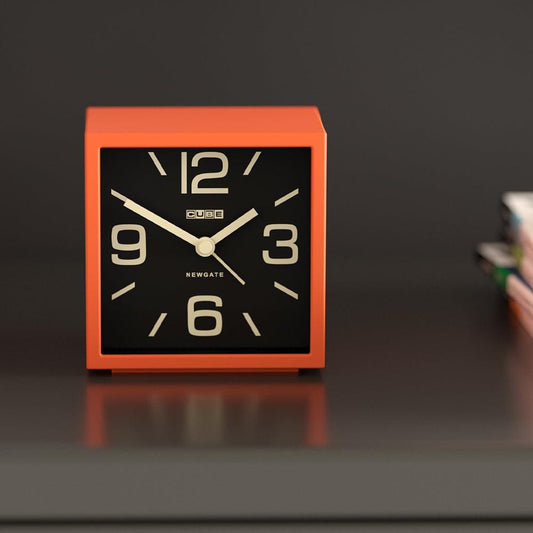 Orange cube mantel clock with black square dial and gold hands, angled view