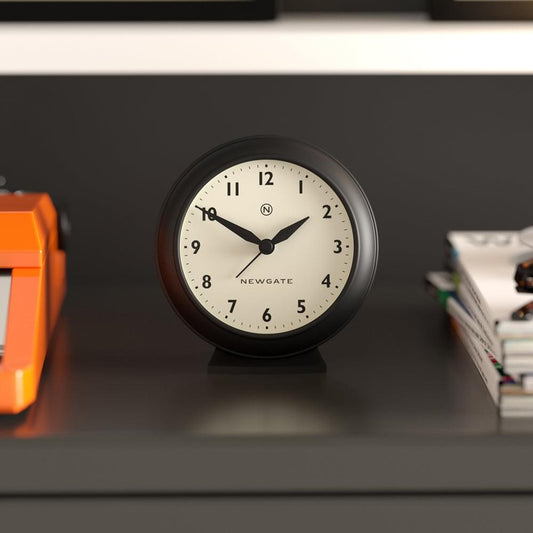 Black mantel clock on shelf, cream face with black hands and numerals, Newgate logo