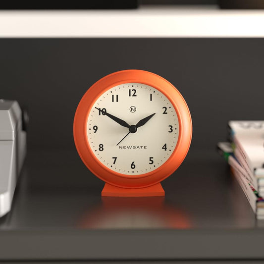Pumpkin orange mantel clock on a shelf, cream face with black hour and minute hands