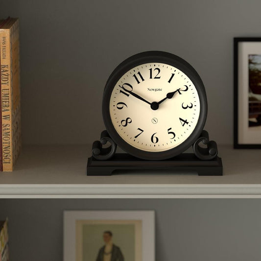 Black mantel clock with cream dial displayed on a shelf