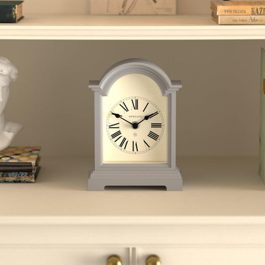 Grey mantel clock on shelf with arched case, cream dial, black Roman numerals and hands