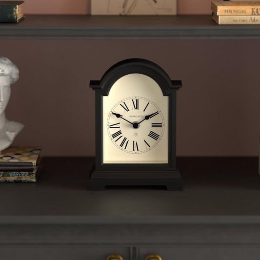 Black mantel clock with arched case, cream dial, Roman numerals, and black hands