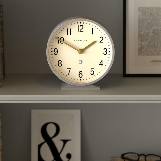 Grey mantel clock on stand with cream dial, Newgate logo, black numbers, gold hands