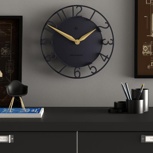 Wall clock on wall with dark dial, gold hands, and black circular frame with oversized numerals