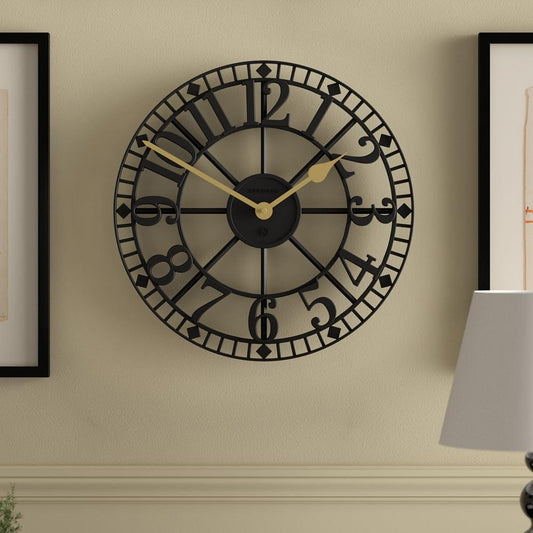 Black round wall clock on wall with Roman-style numerals and gold-tone hands
