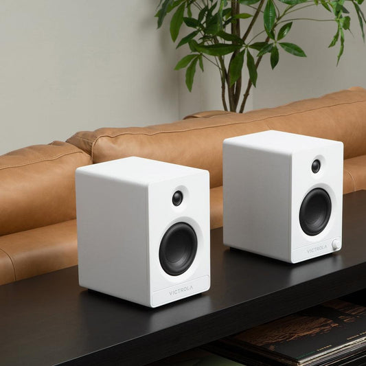 White bookshelf speaker pair on a tabletop, showing front black woofer and tweeter.