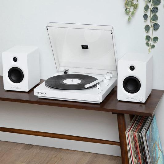White turntable with record and two white bookshelf speakers on a console.