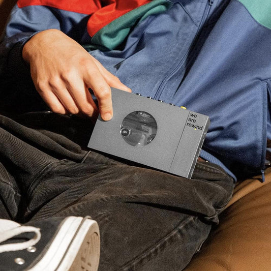Grey cassette player/recorder held on dark fabric with hand