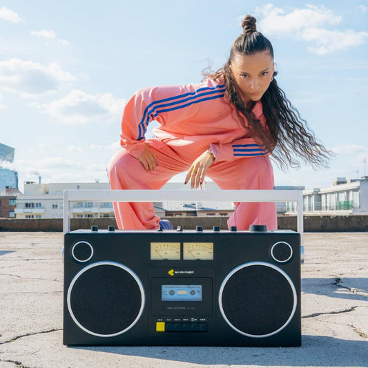 Black cassette player and recorder with large speakers, held on a ledge by a person.