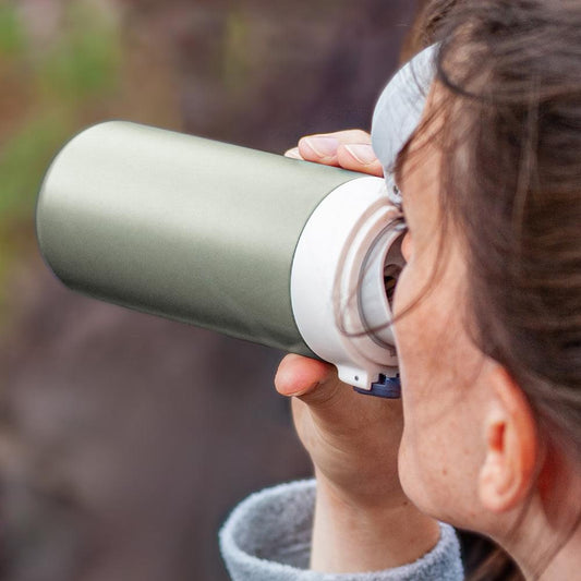 Green insulated bottle tilted for drinking; white mouthpiece and dark-blue button