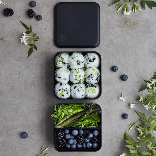 Black square bento box with lid open and two filled food compartments