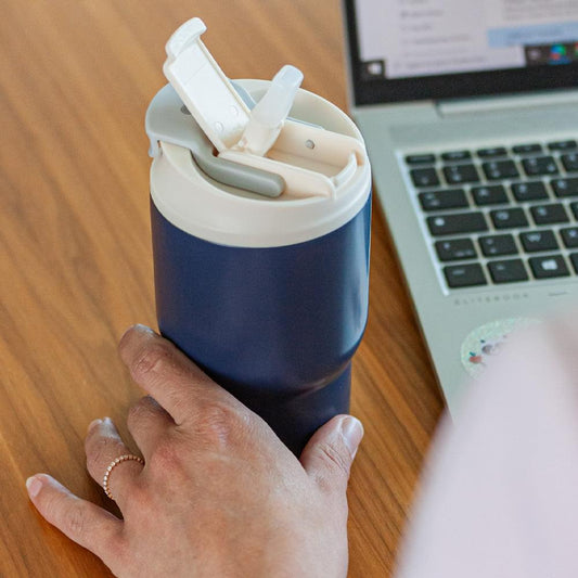 Dark blue insulated travel mug held by hand, lid open with white spout