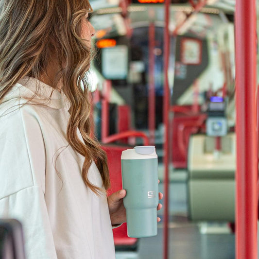 Mint green travel mug with white flip-top lid, held in hand