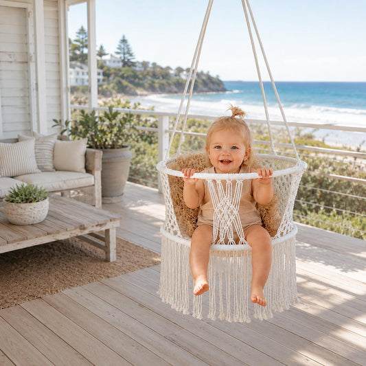 Cream macrame hanging baby swing chair with fringed base and seated child