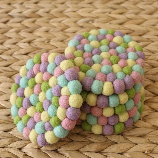 Pastel rainbow wool-felt coaster with rounded ball clusters on woven surface.