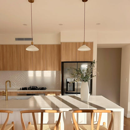 Group of ceramic pleated pendant lights with white shades and brass finishes above island