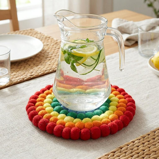 Round rainbow felt pot mat with multicolor looped edge beneath a glass pitcher