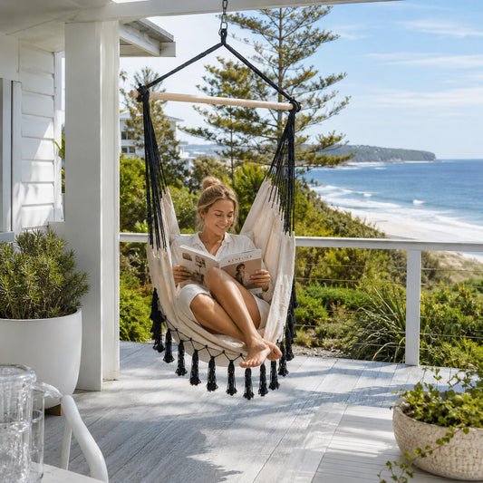 Cream hanging hammock chair with black tassel trim and wooden spread bar.